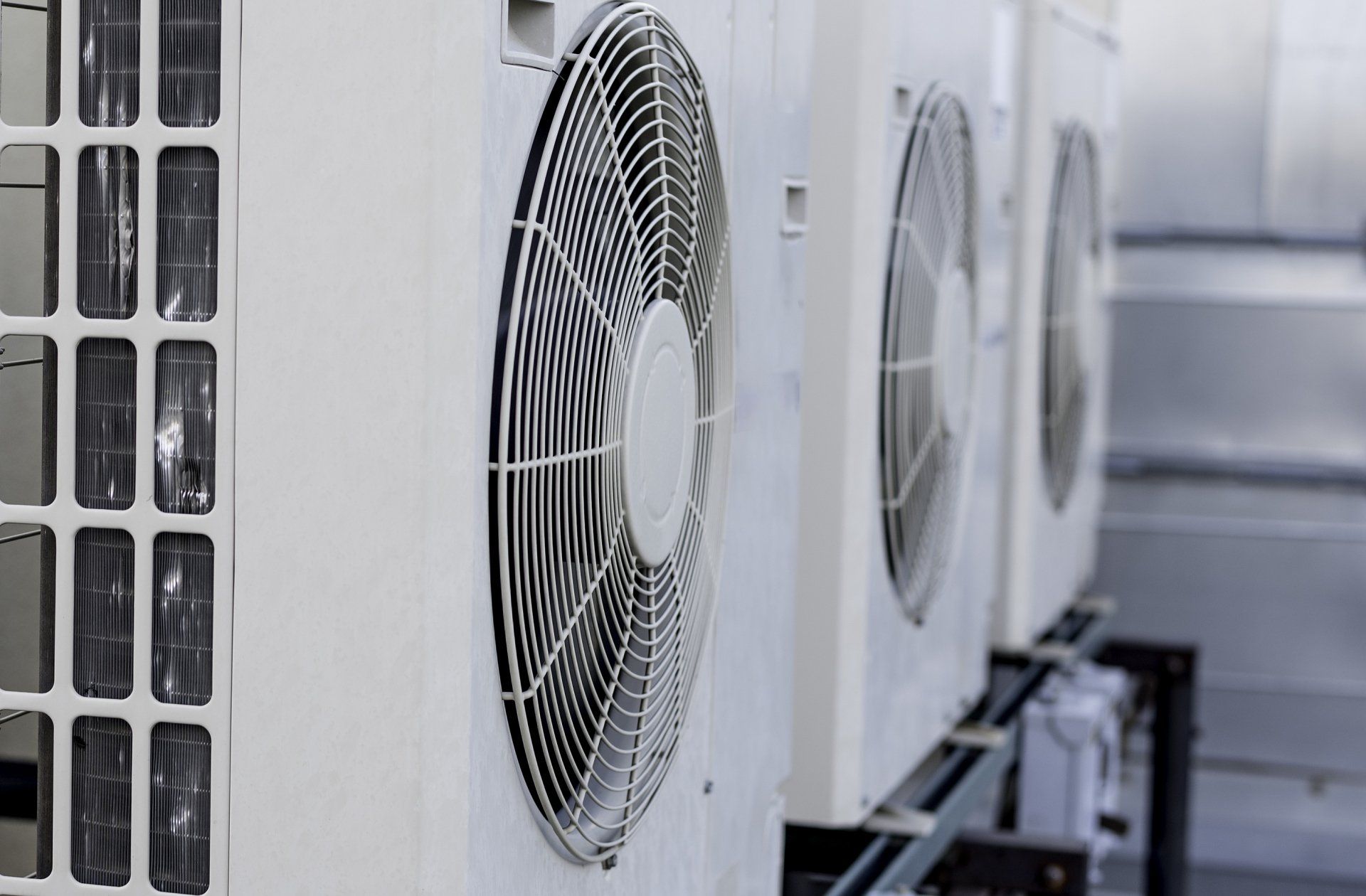 Row of outdoor air conditioning units with large fan grilles along a building wall