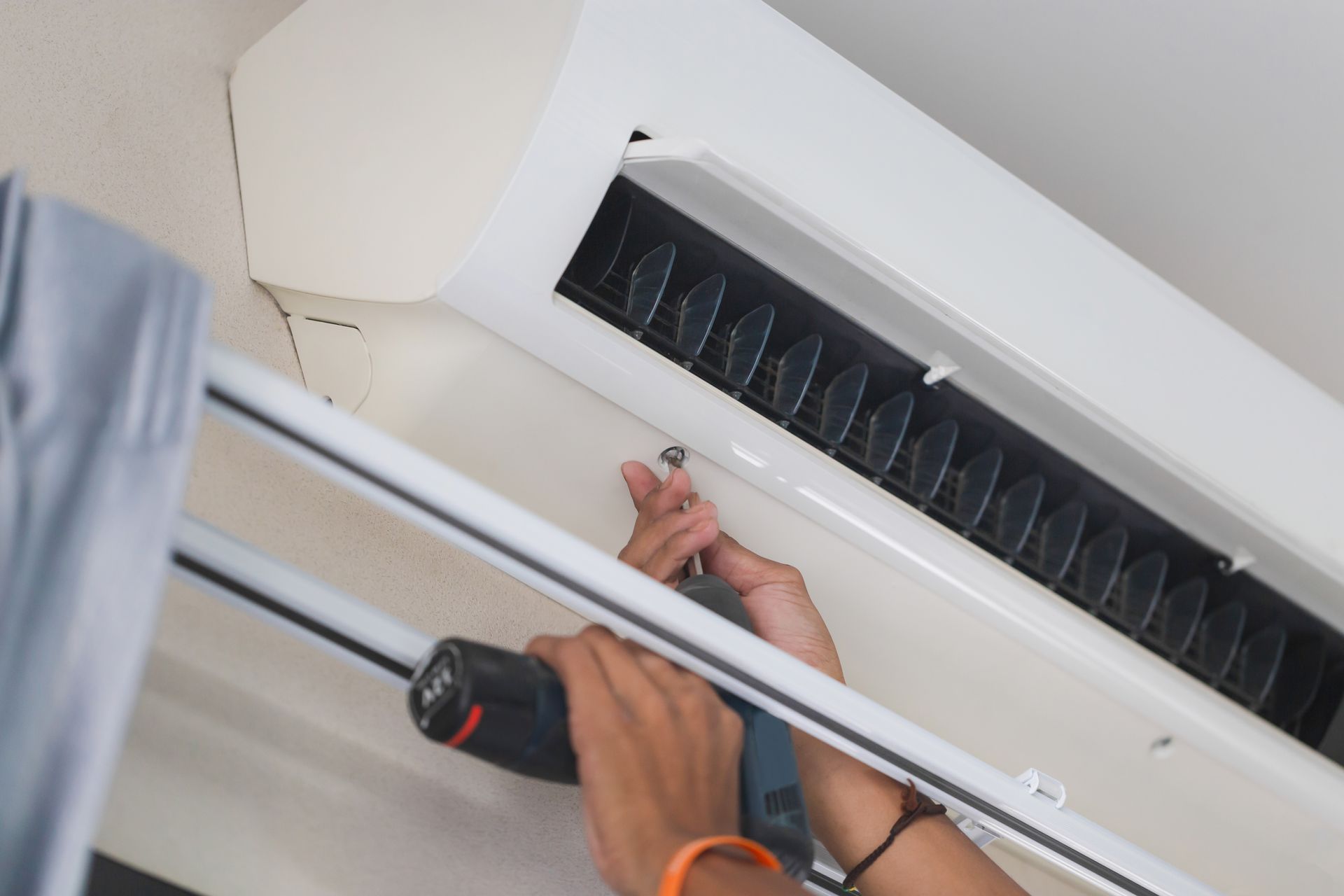 Furnace Installers Near You in Hands using a screwdriver to service a wall-mounted air conditioner.