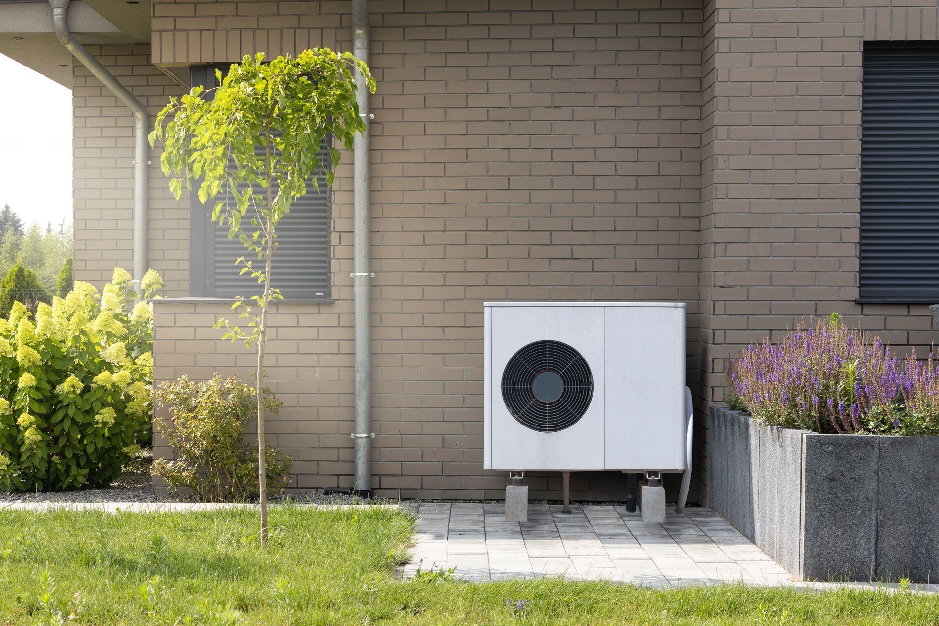 New Furnace Installations in Garner, NC Outdoor home air conditioner unit beside a brick house and garden bed