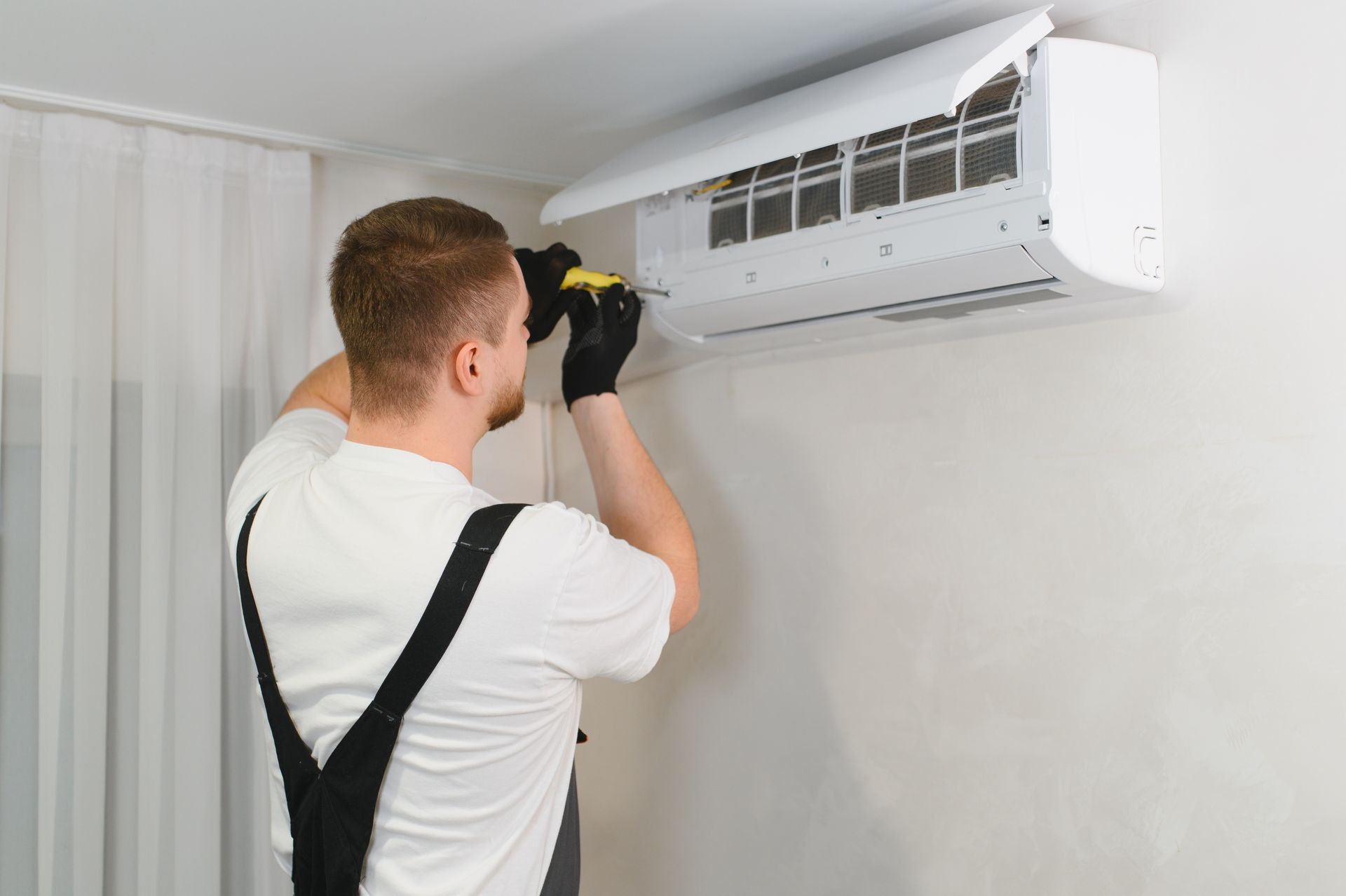 Technician adjusting a wall-mounted air conditioner with a screwdriver in a white room