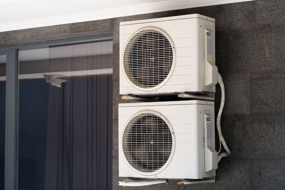 Mini Splits in Holly Springs, NC Two stacked outdoor air conditioner units mounted on a building wall near a window