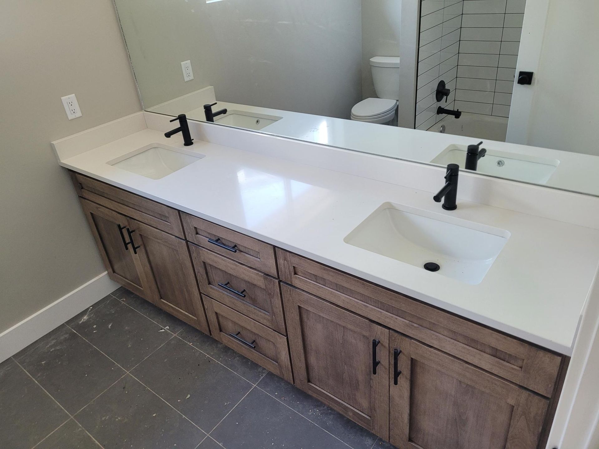 Double vanity with white countertop, brown cabinets, black faucets, and large mirror.