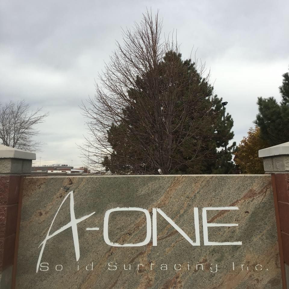 Sign for A-ONE Solid Surfacing Inc. on stone; cloudy sky and trees in the background.