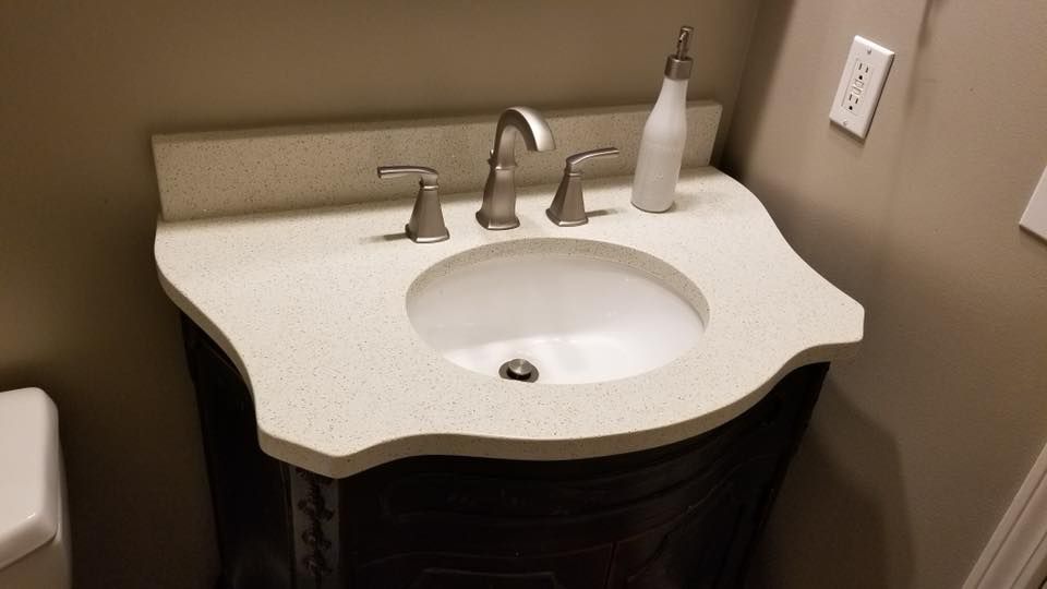 Bathroom vanity with white sink, beige countertop, and silver faucet on a dark cabinet.