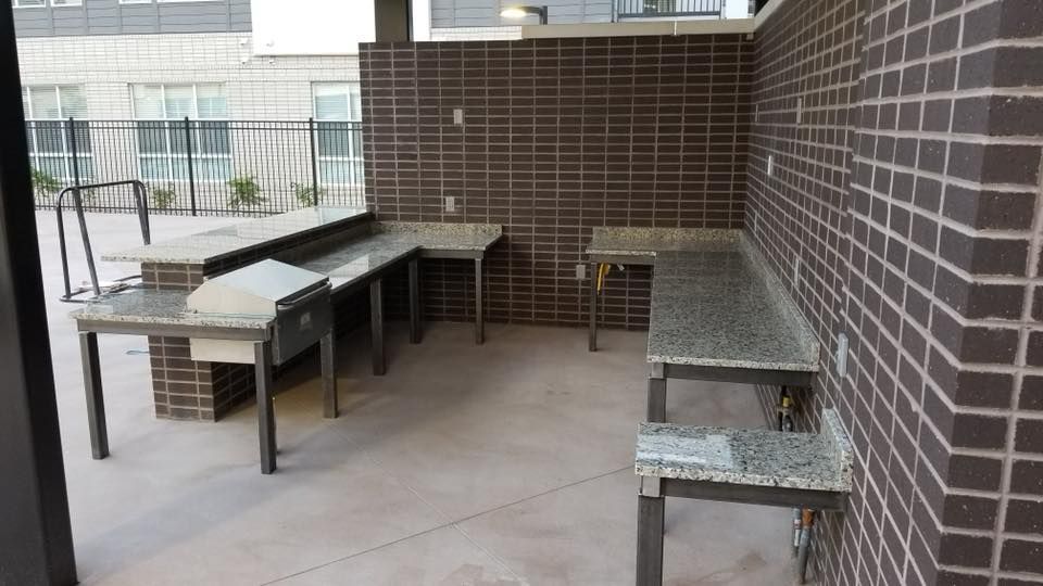 Outdoor grilling area with brick walls, metal tables with granite countertops.