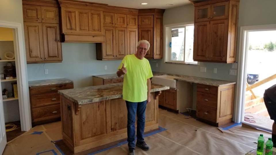 Man in neon green shirt gives thumbs up in a kitchen with wooden cabinets and granite countertops.