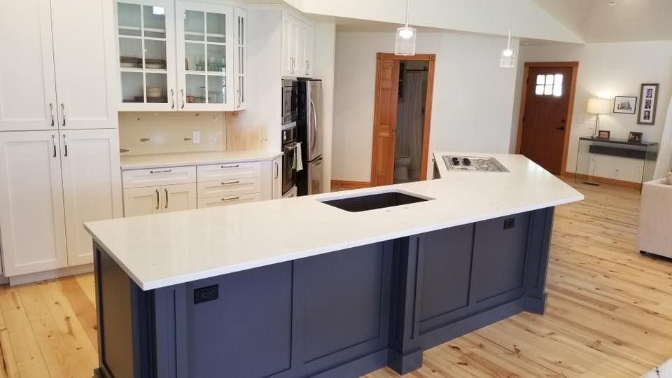 Modern kitchen with white cabinets, dark blue island, and light wood floors.