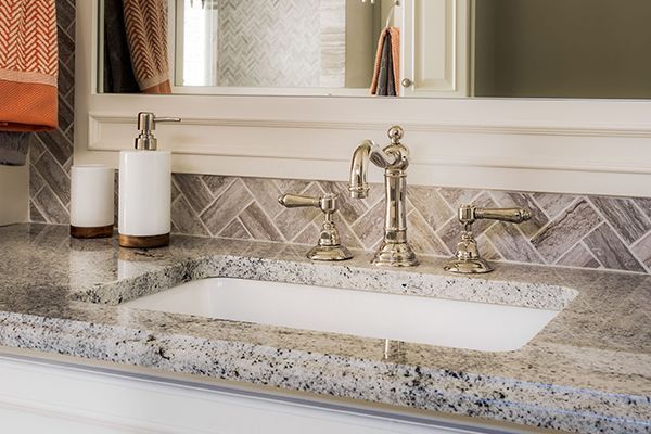 Bathroom sink with granite countertop and gray backsplash.