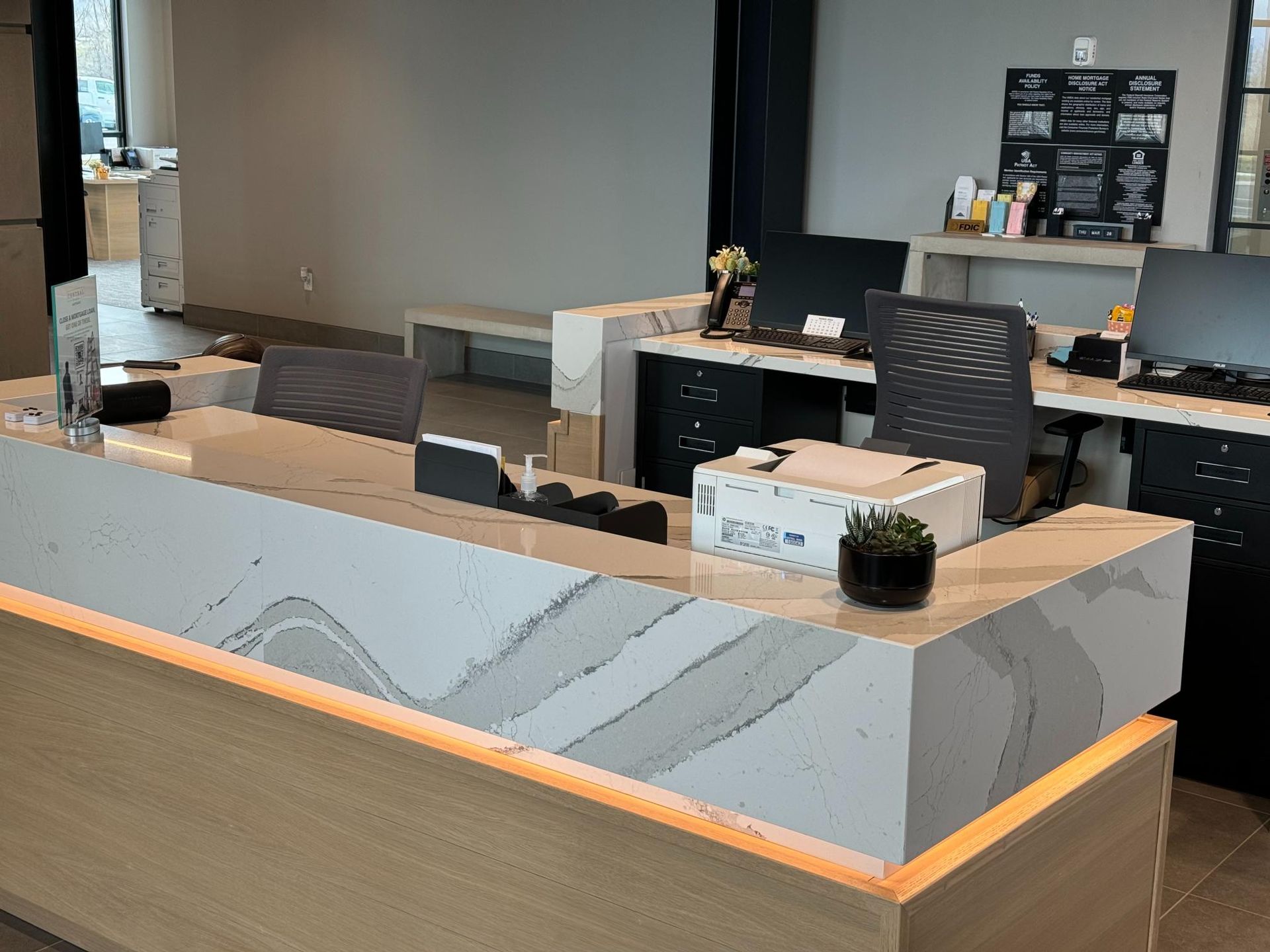 Reception desk with marble countertop and computers, small plant, and printer.