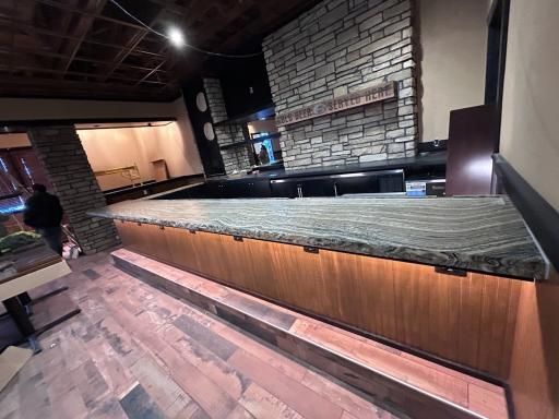 Bar with granite countertop, wood paneling, and stone accents; a person walks in the background.