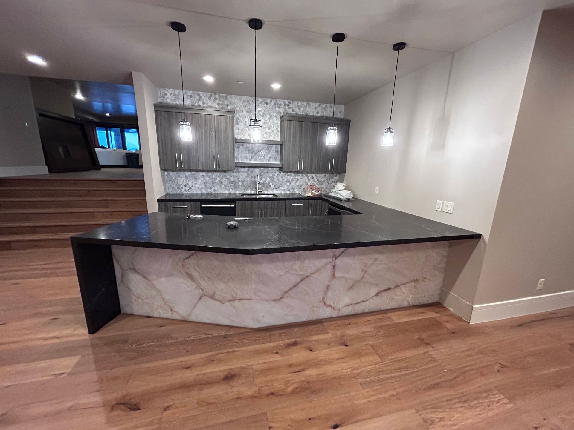 A modern bar with black countertop, gray cabinets, and light wood flooring.