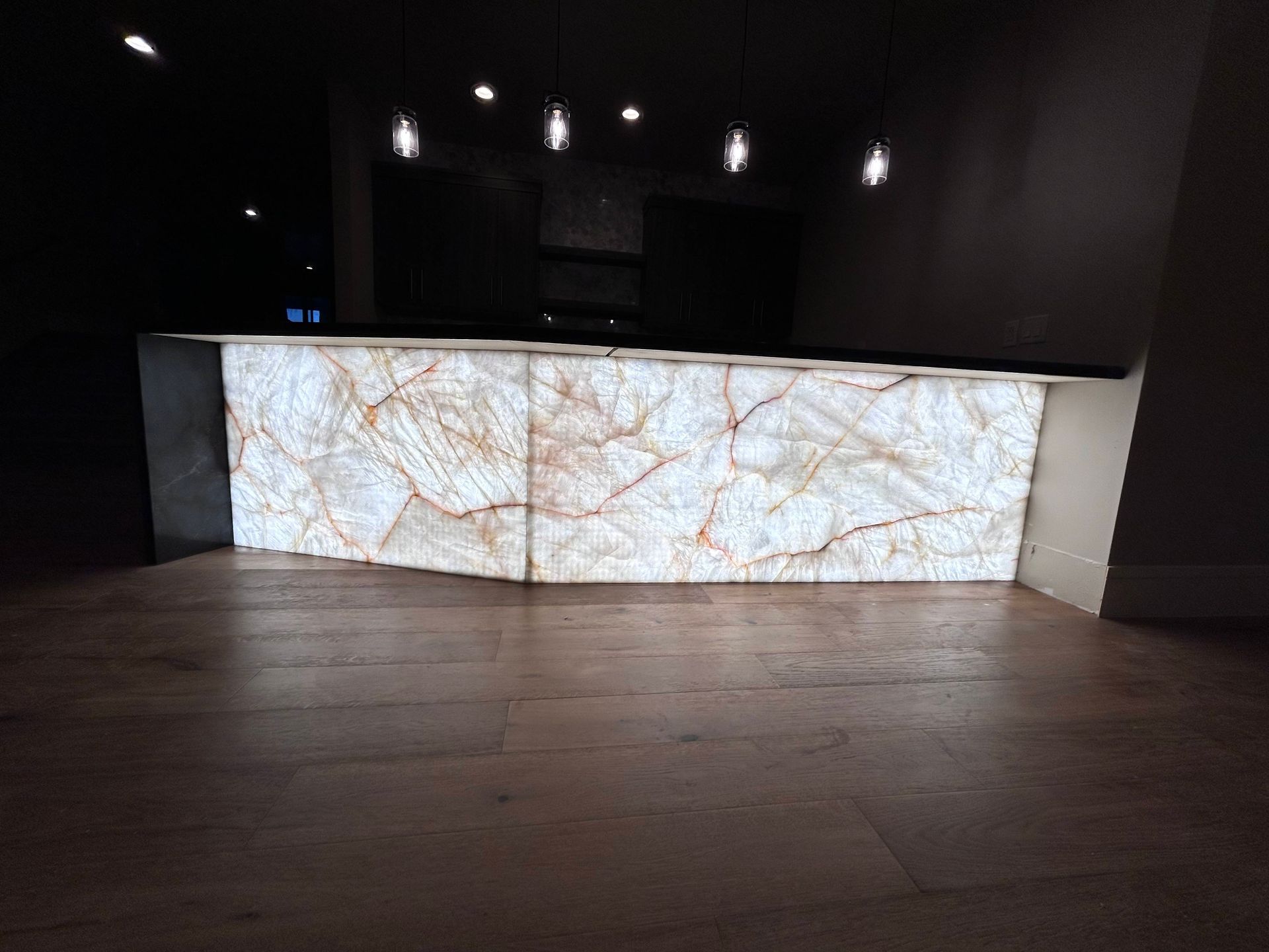 Lit kitchen island with brown veined, glowing surface, against a dark background, wooden floor.