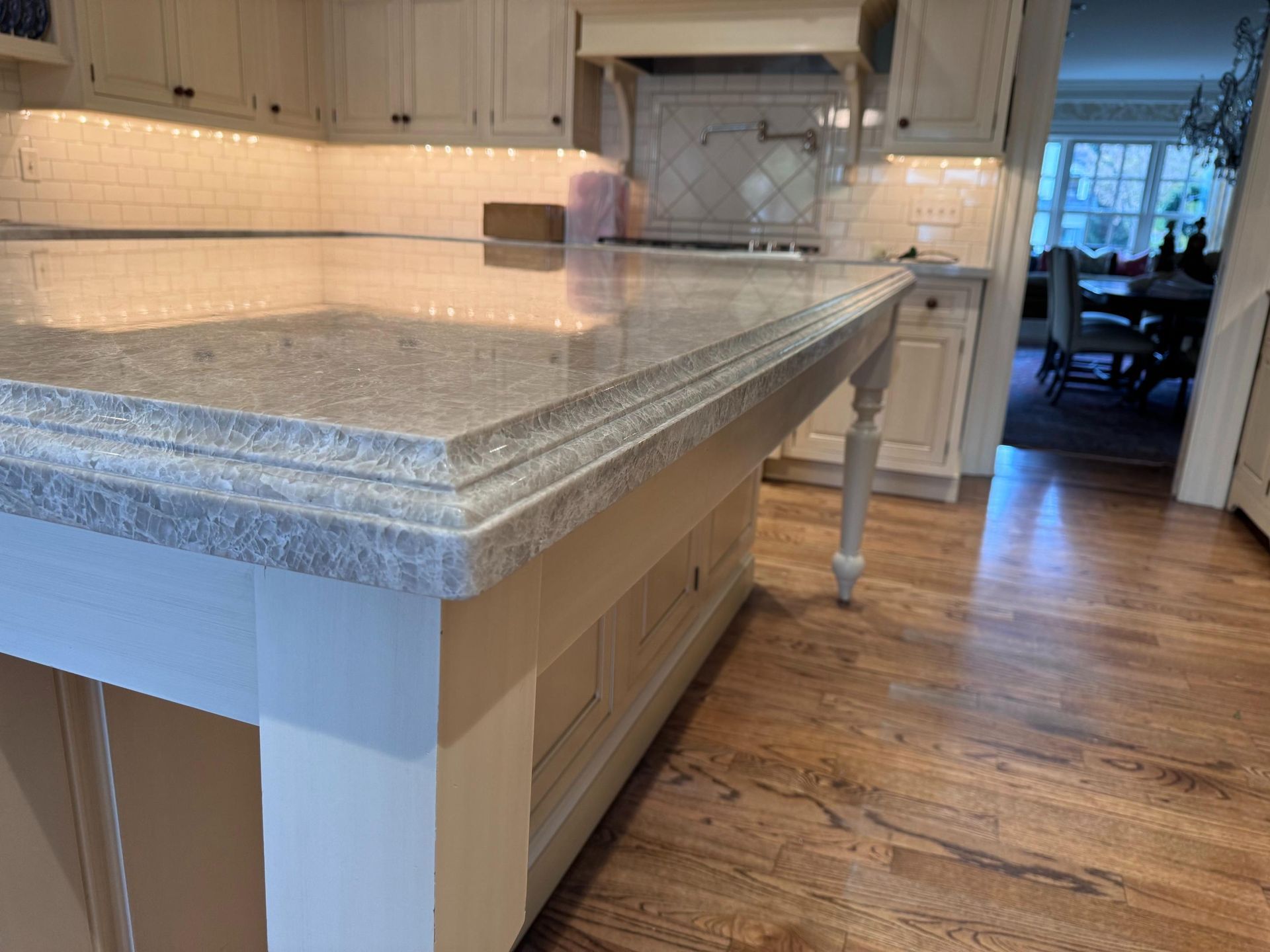 Cream-colored kitchen island with gray granite countertop, wood floor, and overhead cabinets.