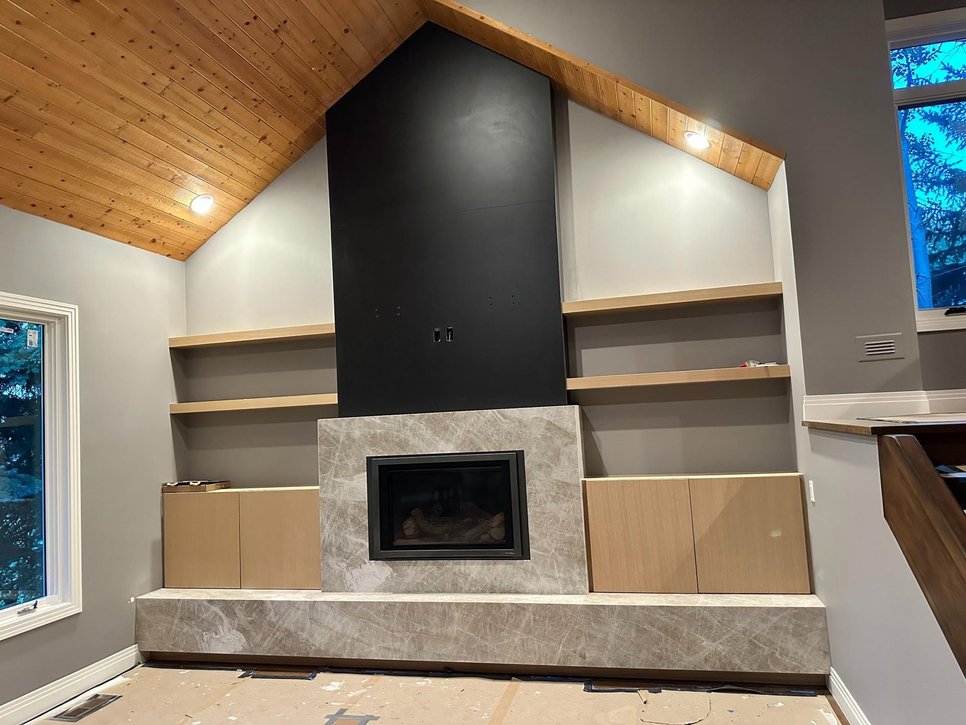 Fireplace with black surround and stone facade, flanked by shelves and cabinets. Wooden ceiling.