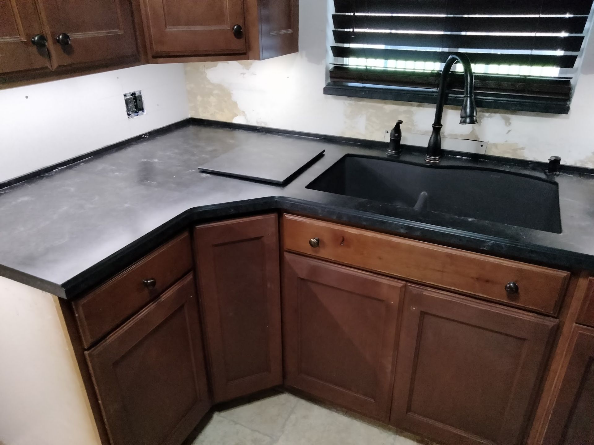 Kitchen corner with dark countertops, cabinets, and a black sink under a window.