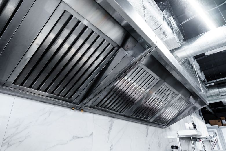 Stainless steel kitchen exhaust hoods and vents above white tiled walls in a commercial kitchen