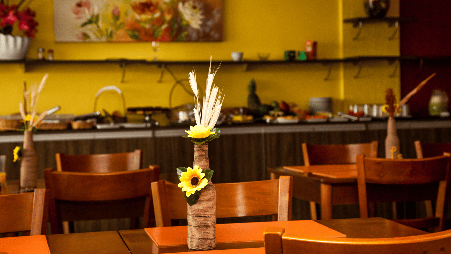 Um restaurante com mesas e cadeiras e um vaso de flores sobre a mesa.
