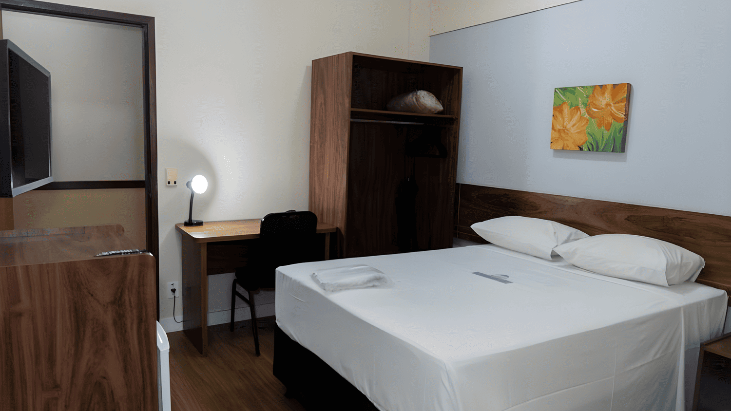 Um quarto de hotel com uma cama, escrivaninha, cadeira e televisão.