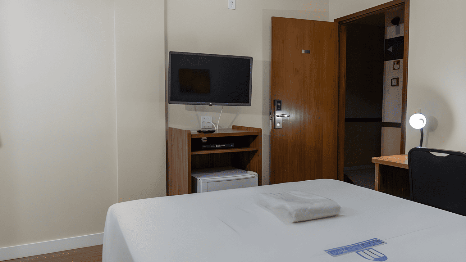 Um quarto de hotel com cama, televisão e geladeira.