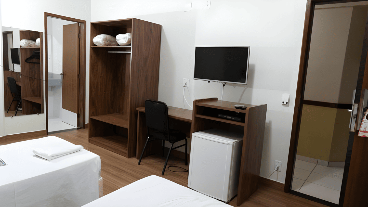 Um quarto de hotel com duas camas, uma escrivaninha, uma televisão e uma geladeira.
