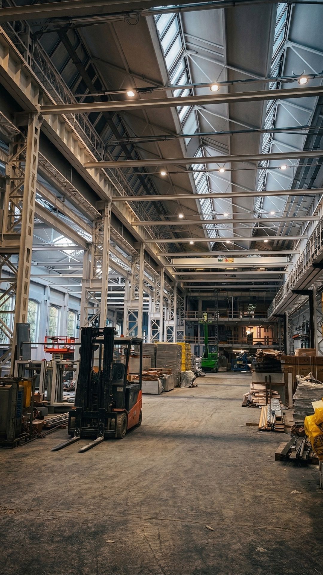 All'interno di un grande magazzino industriale con travi in ​​acciaio, lucernari, macchinari e un pavimento in cemento.