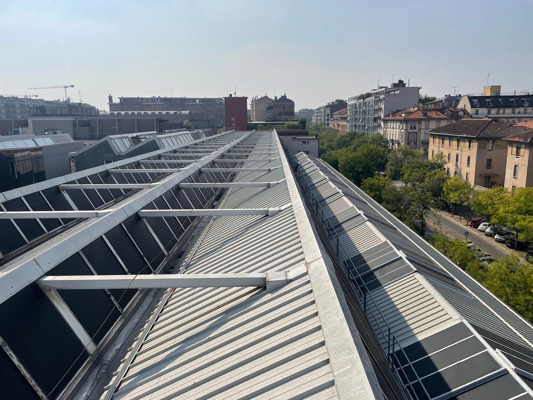 Pannelli solari sul tetto di un grande edificio che si affaccia su una strada cittadina e sui tetti circostanti.