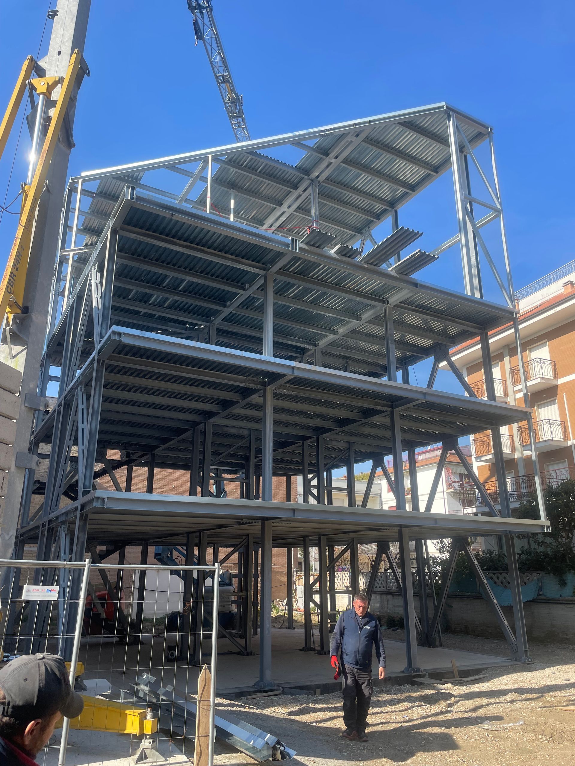 Edificio con struttura in acciaio in costruzione, con operai e una gru sul posto.