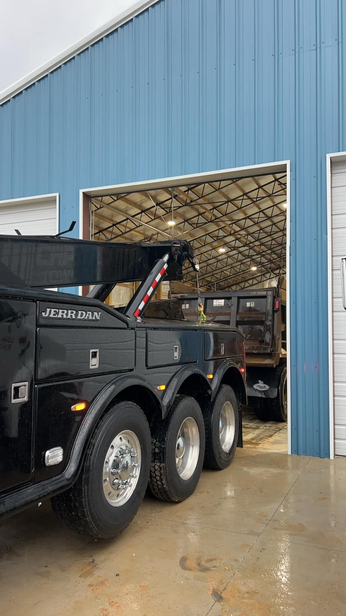 Black dump truck backed into a blue warehouse entrance on a wet concrete floor.