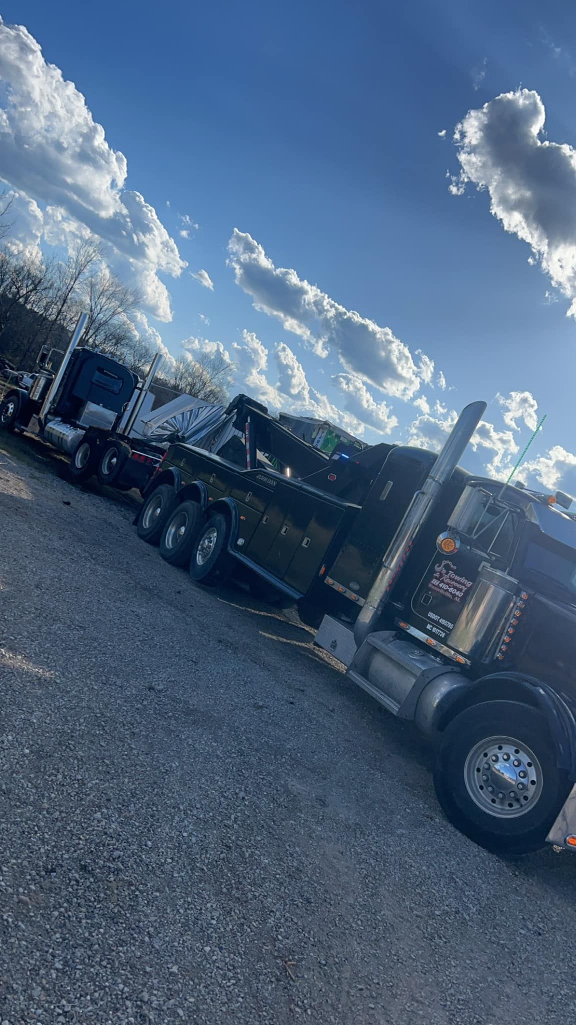 Black semi-truck parked on gravel under a bright blue sky with clouds.