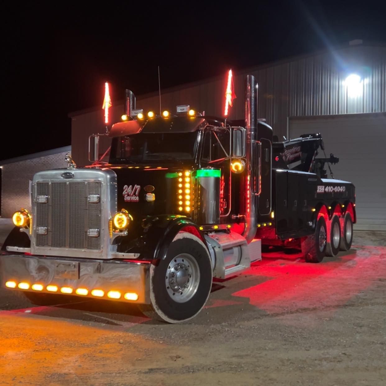 Black semi truck with red lights parked at night on a lot