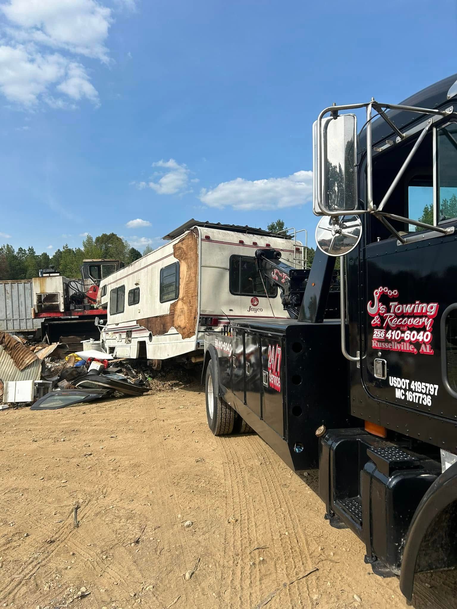 Tow truck beside a damaged RV on a gravel lot under a blue sky