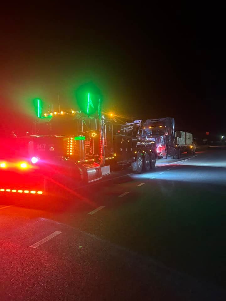 Tow truck with flashing red and green lights towing a disabled truck at night on a highway