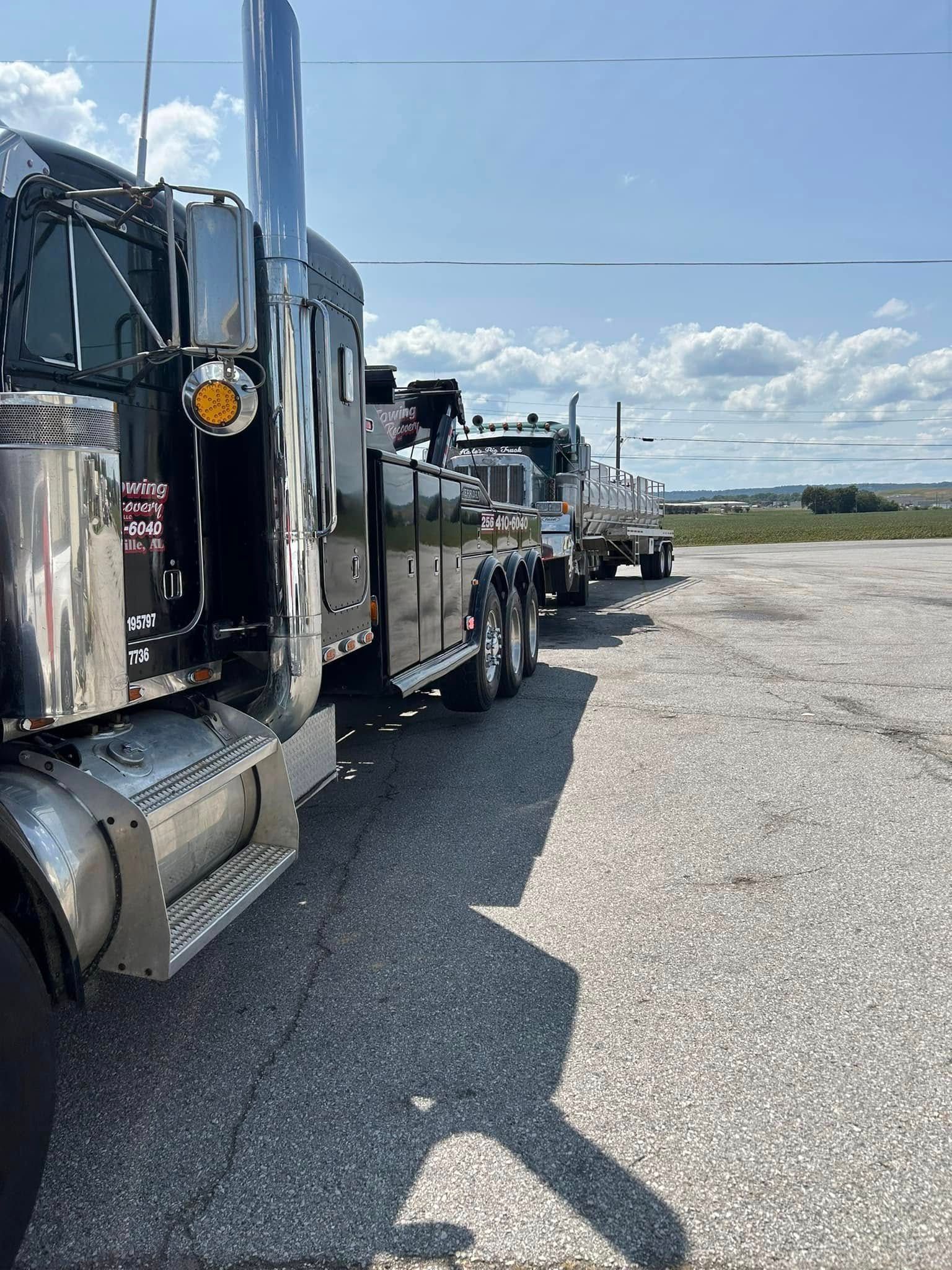 Line of black semi-trucks parked on a gravel lot under a bright blue sky