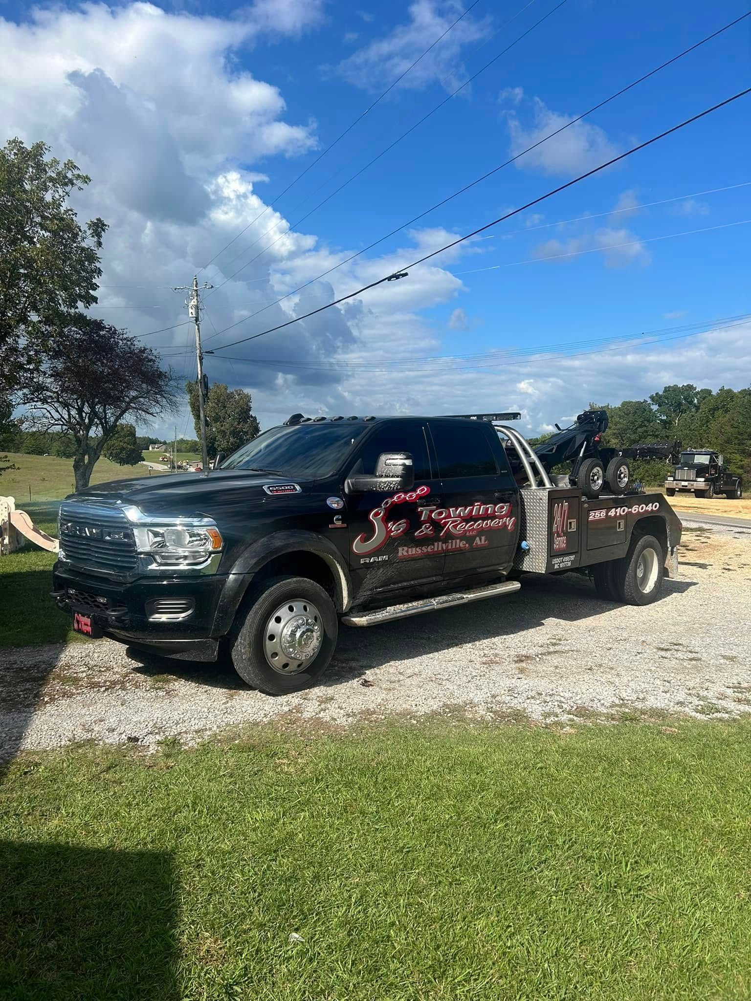 Black pickup truck with red graphics parked on gravel under a blue sky, with grass and trees nearby