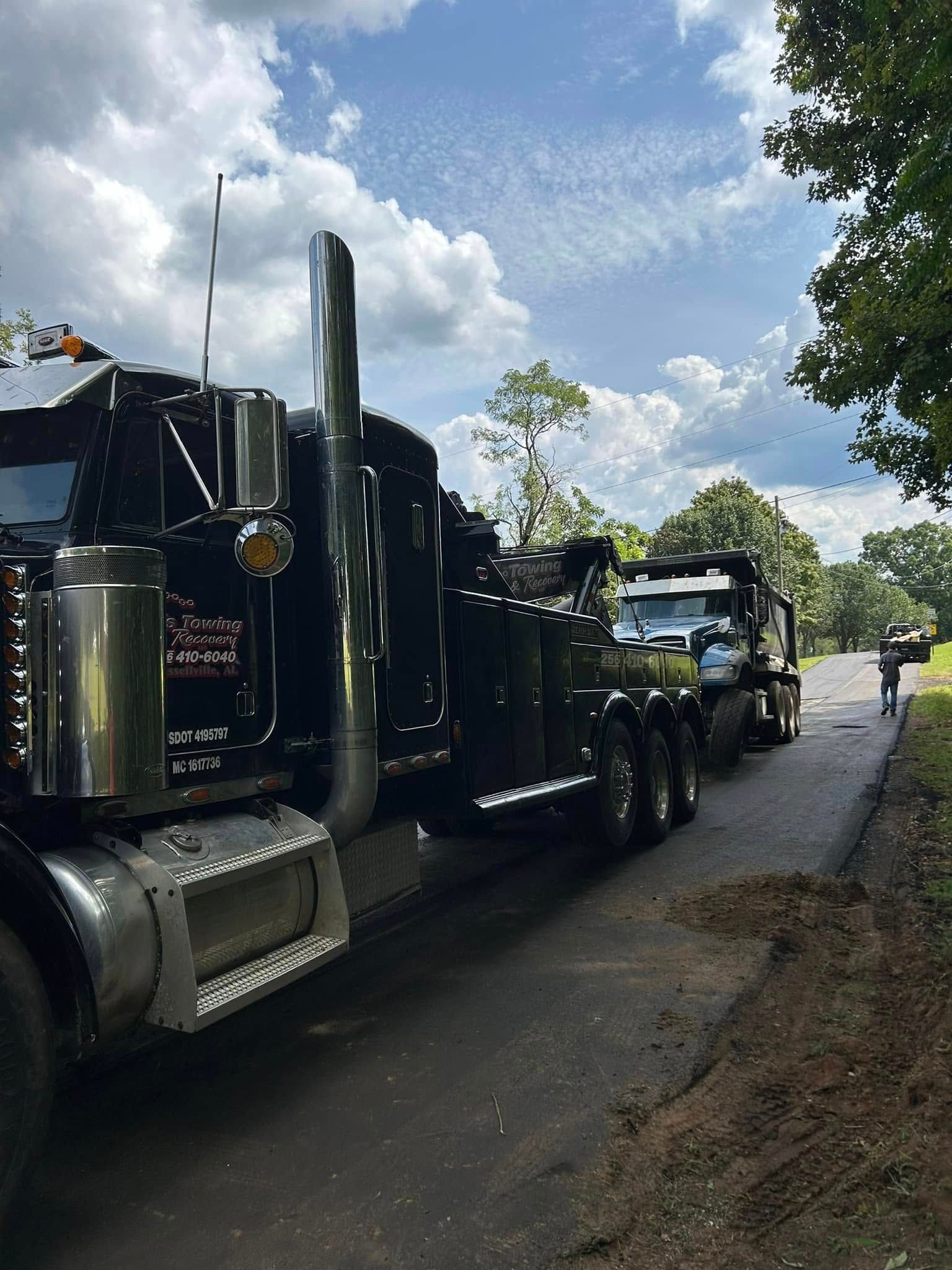 Black semi truck parked on a roadside under a cloudy sky, with another truck behind it.