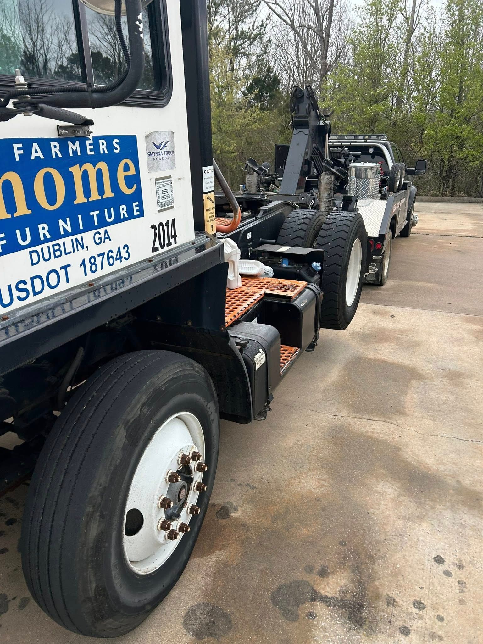 Tow truck hauling a black ATV on a dirt roadside, with a white truck cab in front