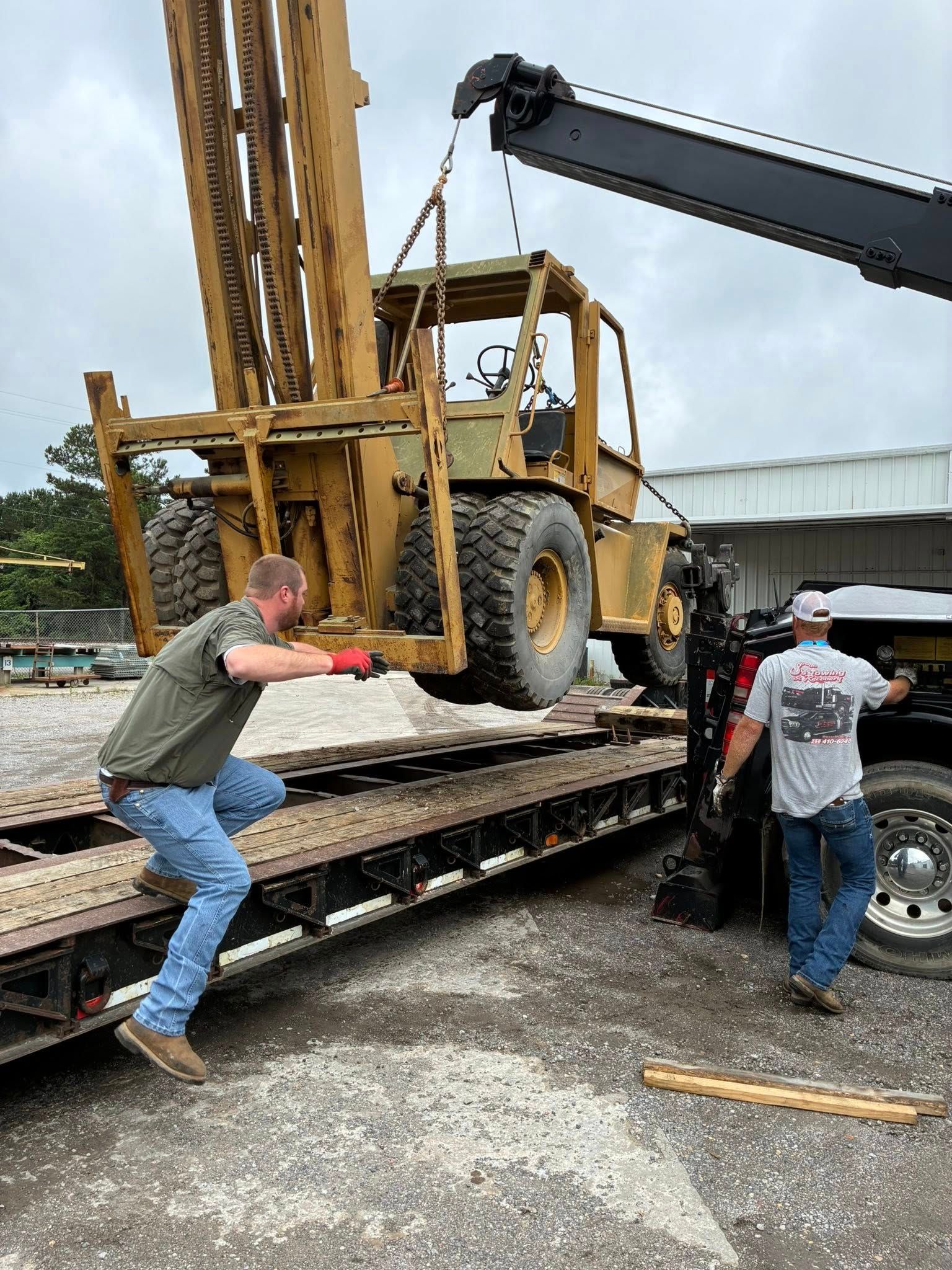 Workers and a crane loading a large yellow drilling rig onto a flatbed truck outdoors