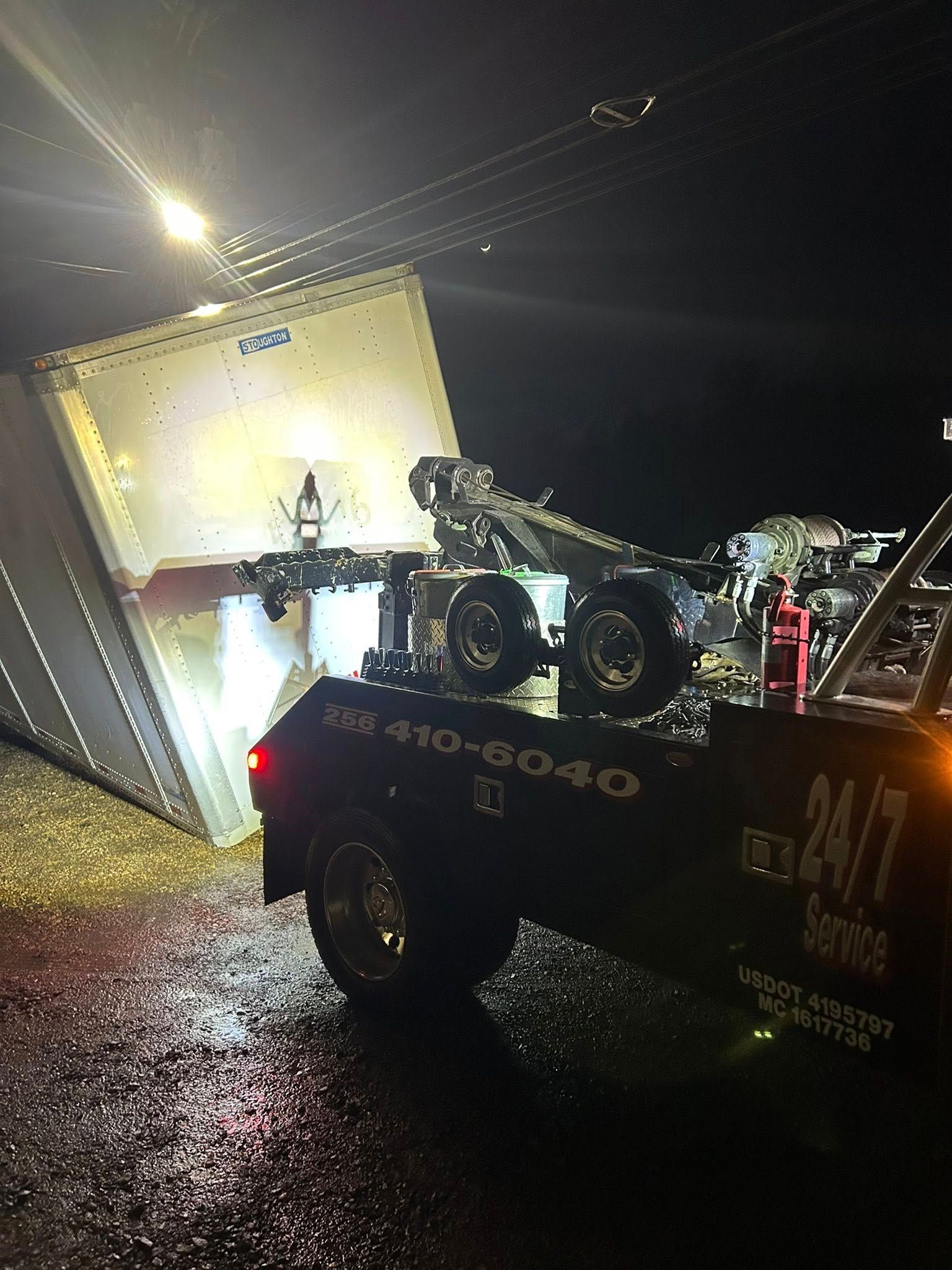 Tow truck pulling an overturned white trailer at night on a wet road
