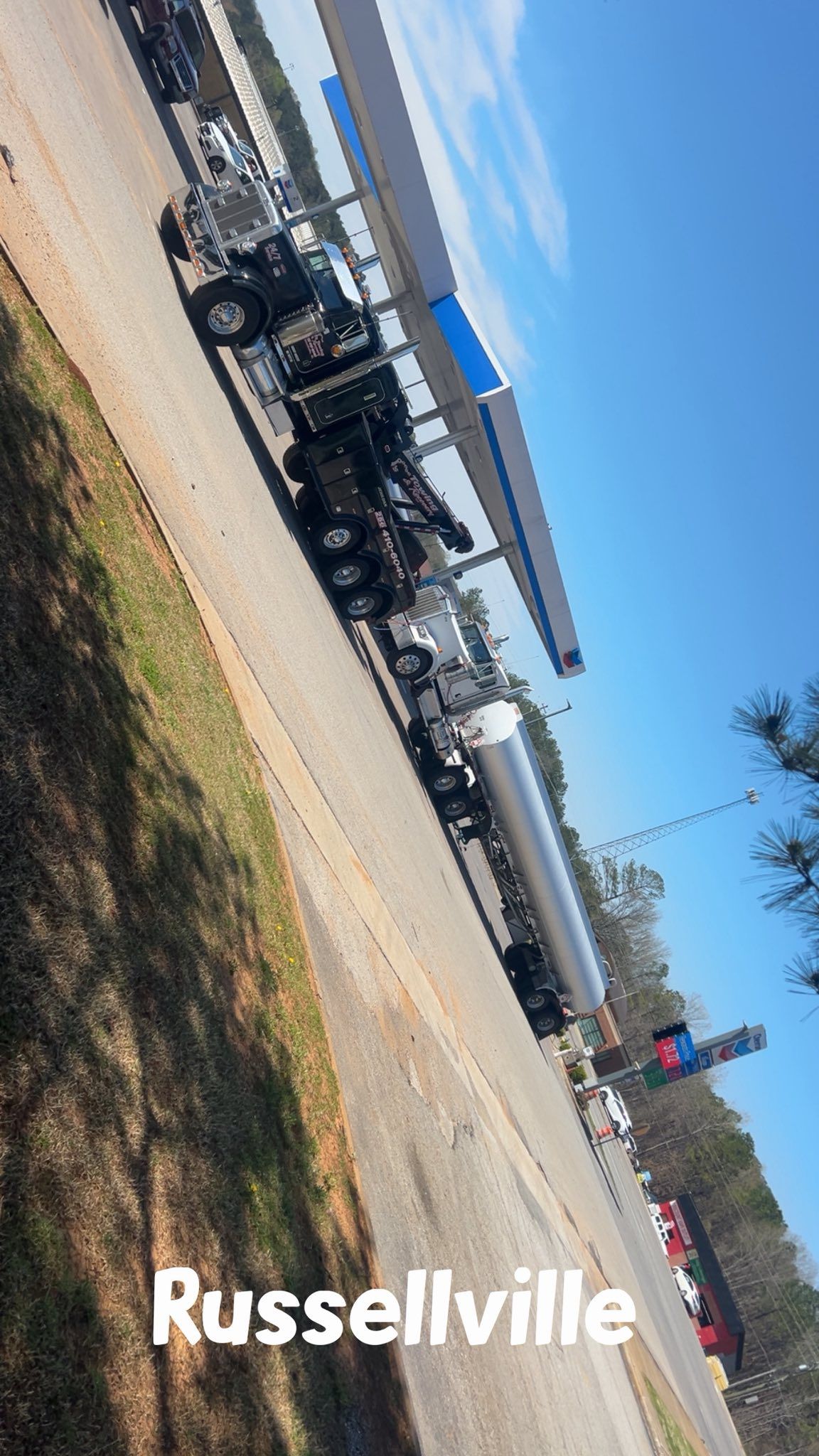 Military vehicles parked along a roadside near a blue-roofed building in Russellville under a clear sky