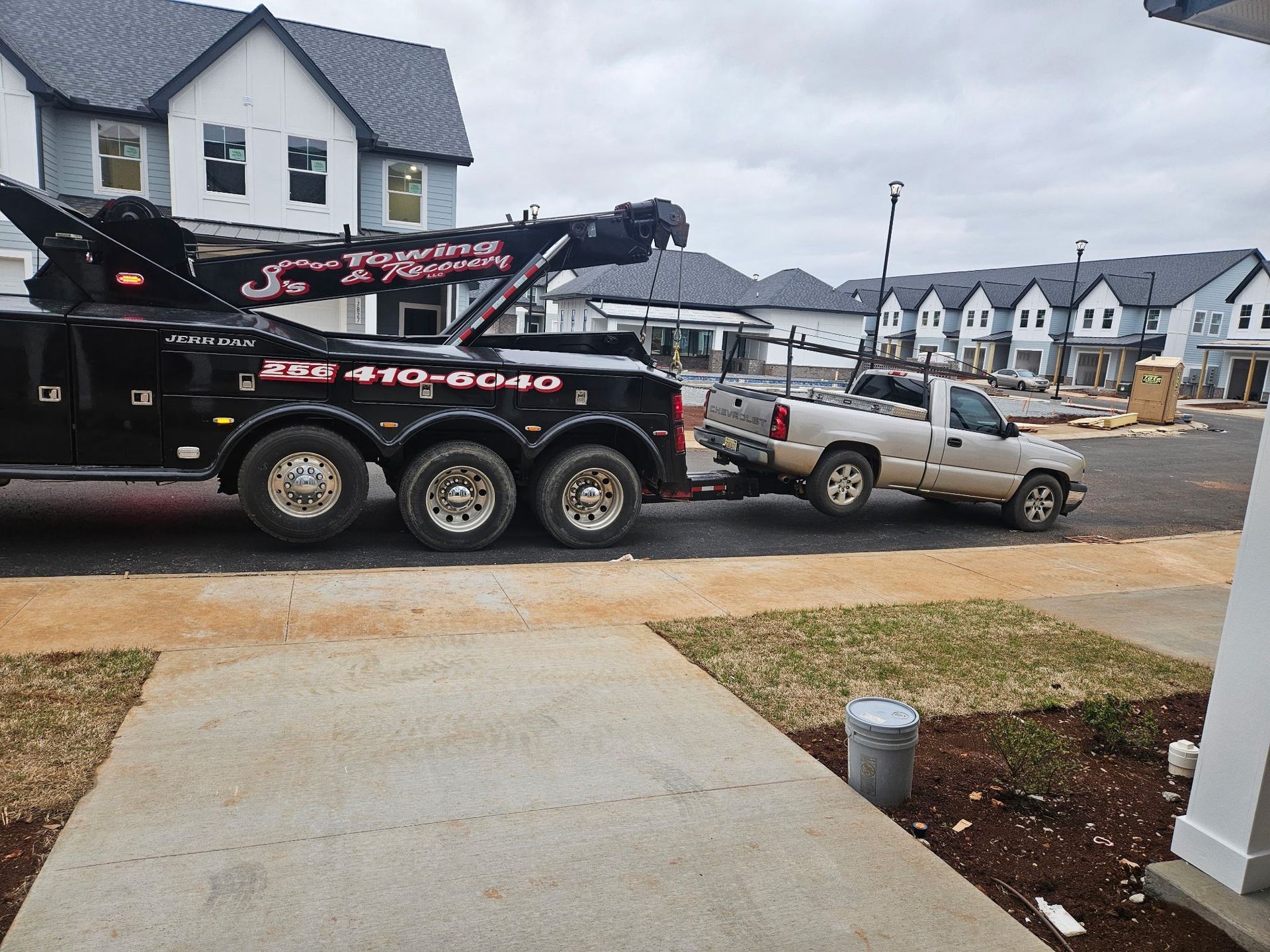 Tow truck towing a pickup truck in a suburban neighborhood with houses and construction in the background