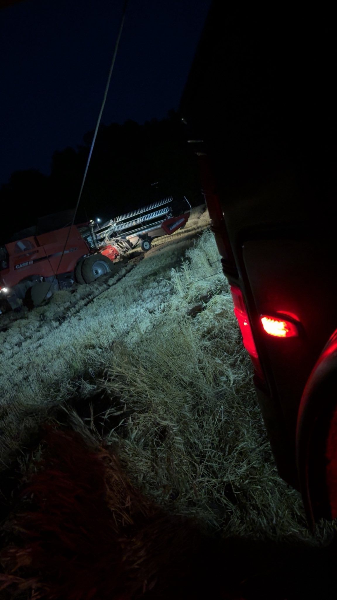 Nighttime roadside scene with a red vehicle, headlights, and a pickup truck on a grassy shoulder.