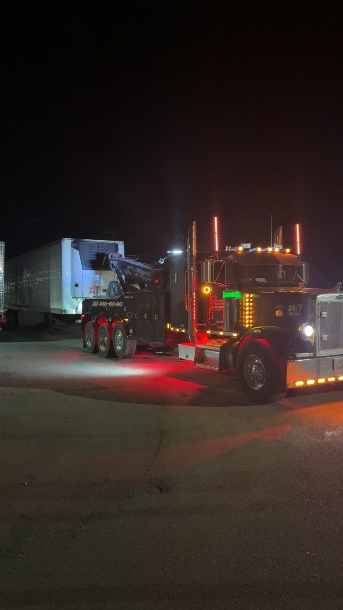 Red semi-truck with lights parked at night beside a white trailer