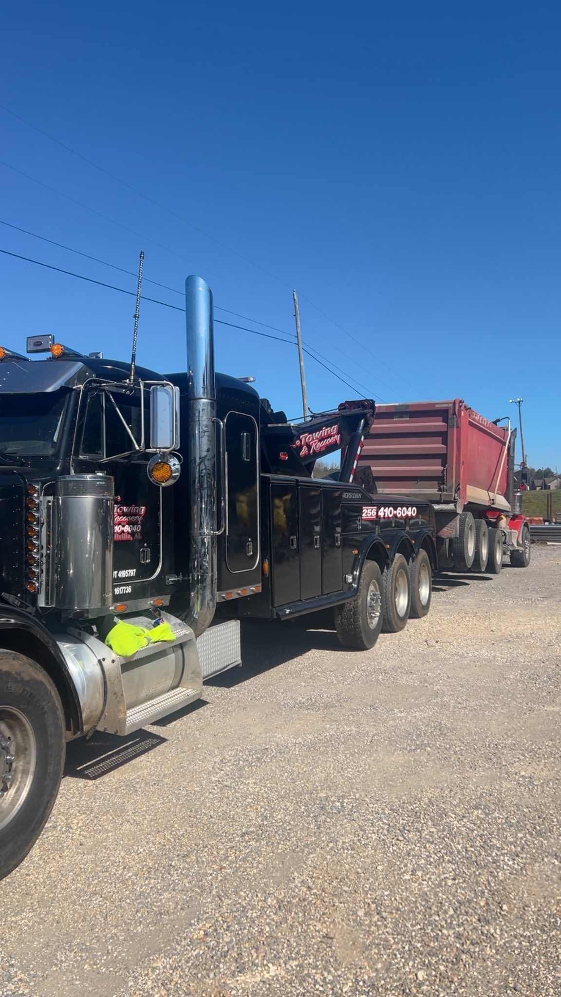 Black semi truck hauling a red dump trailer on a gravel lot under a clear blue sky
