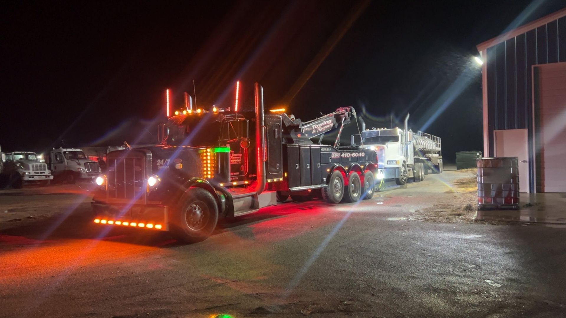 Truck with bright red lights parked at night in a gravel lot beside a building