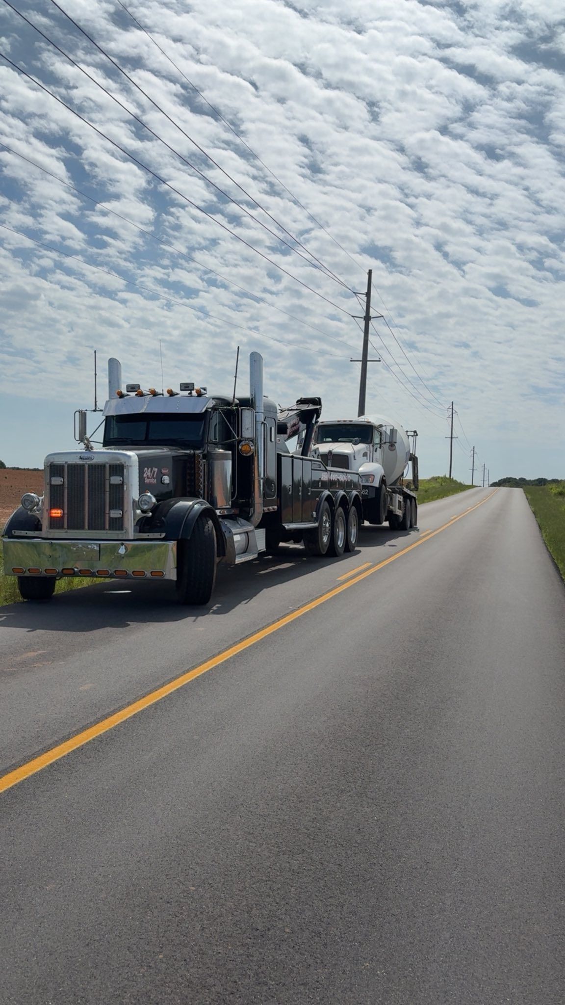 Two semi trucks parked on a rural highway shoulder under a cloudy sky
