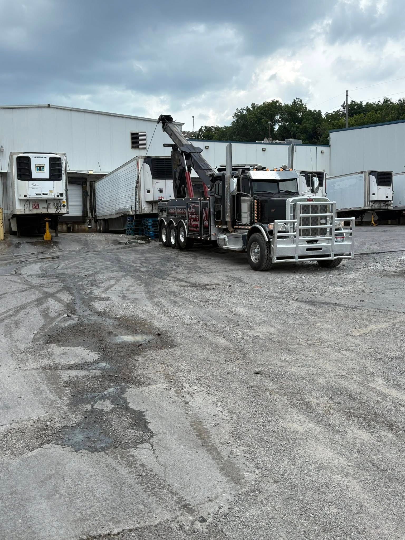 Two semi trucks parked on a gravel lot beside white warehouse trailers