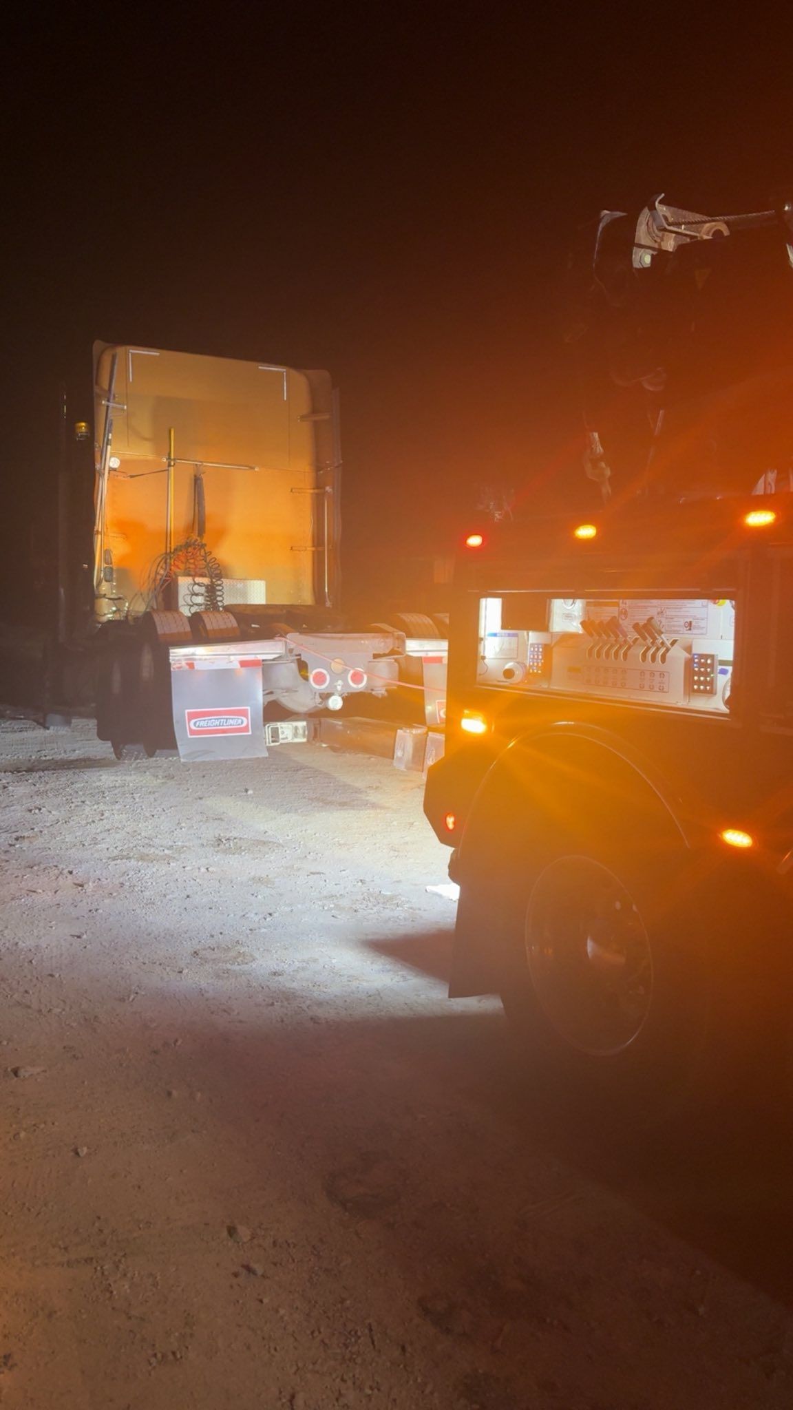 Nighttime street with a truck and bright headlights illuminating a dusty road and building.