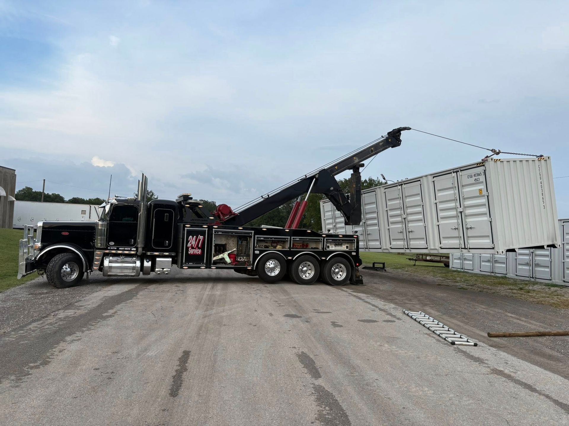 Black tow truck with raised boom on a road beside a white industrial building.