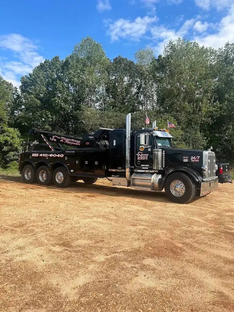 Black dump truck parked on dry dirt with trees and blue sky in the background