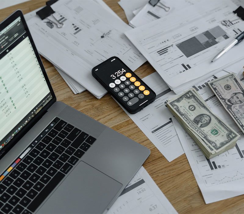 Laptop, calculator, documents, and cash on a wooden desk, suggesting financial calculations or budgeting.